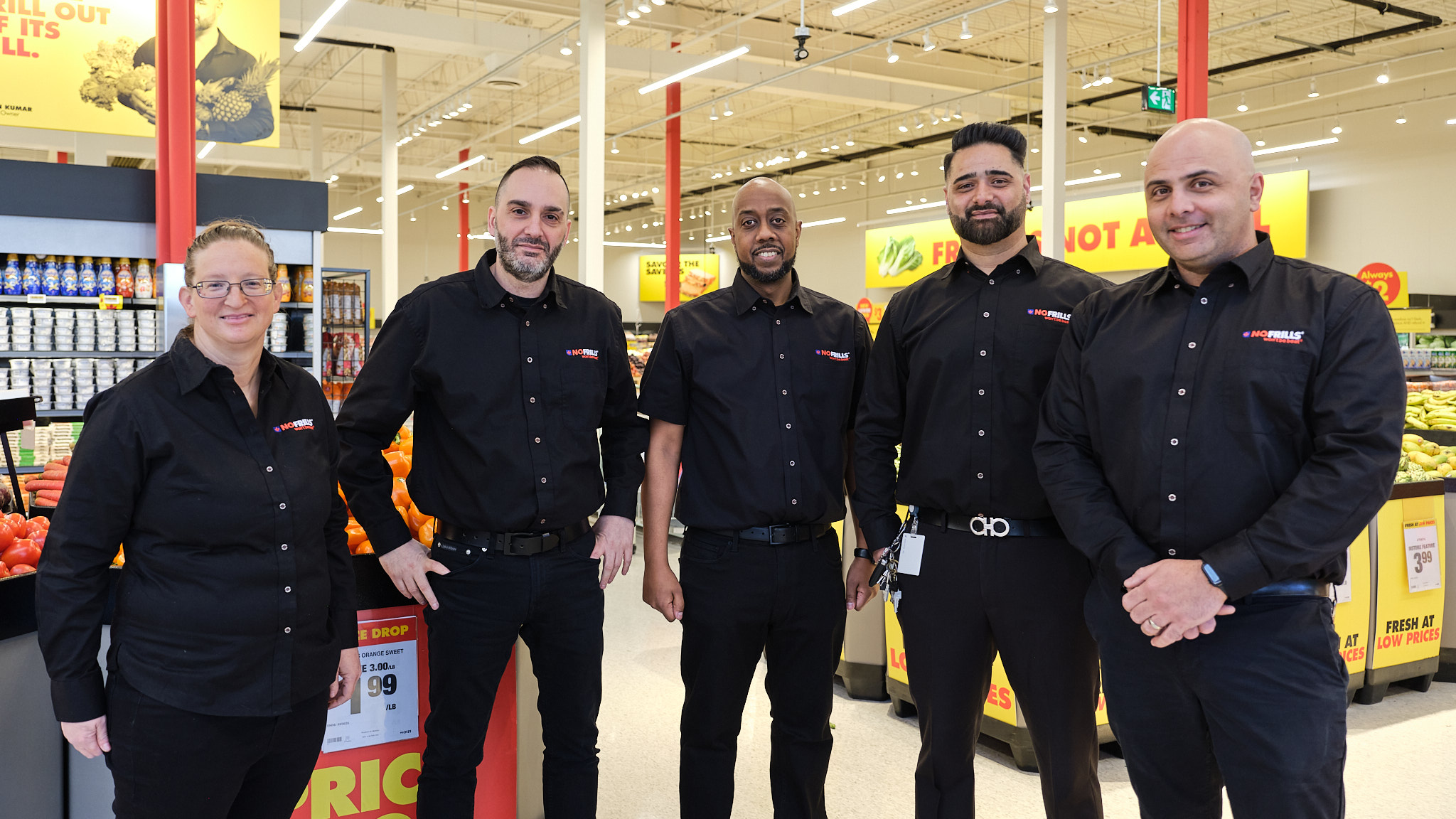 A team of four No&nbsp;Frills employees is posing and smiling in a produce aisle.