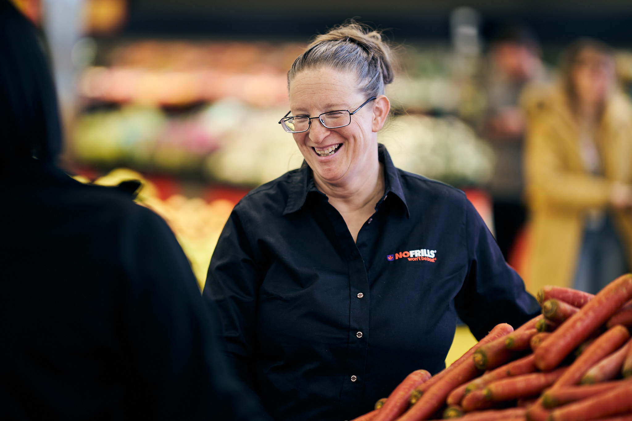 A friendly No&nbsp;Frills employee is smiling while stocking produce in a grocery store.