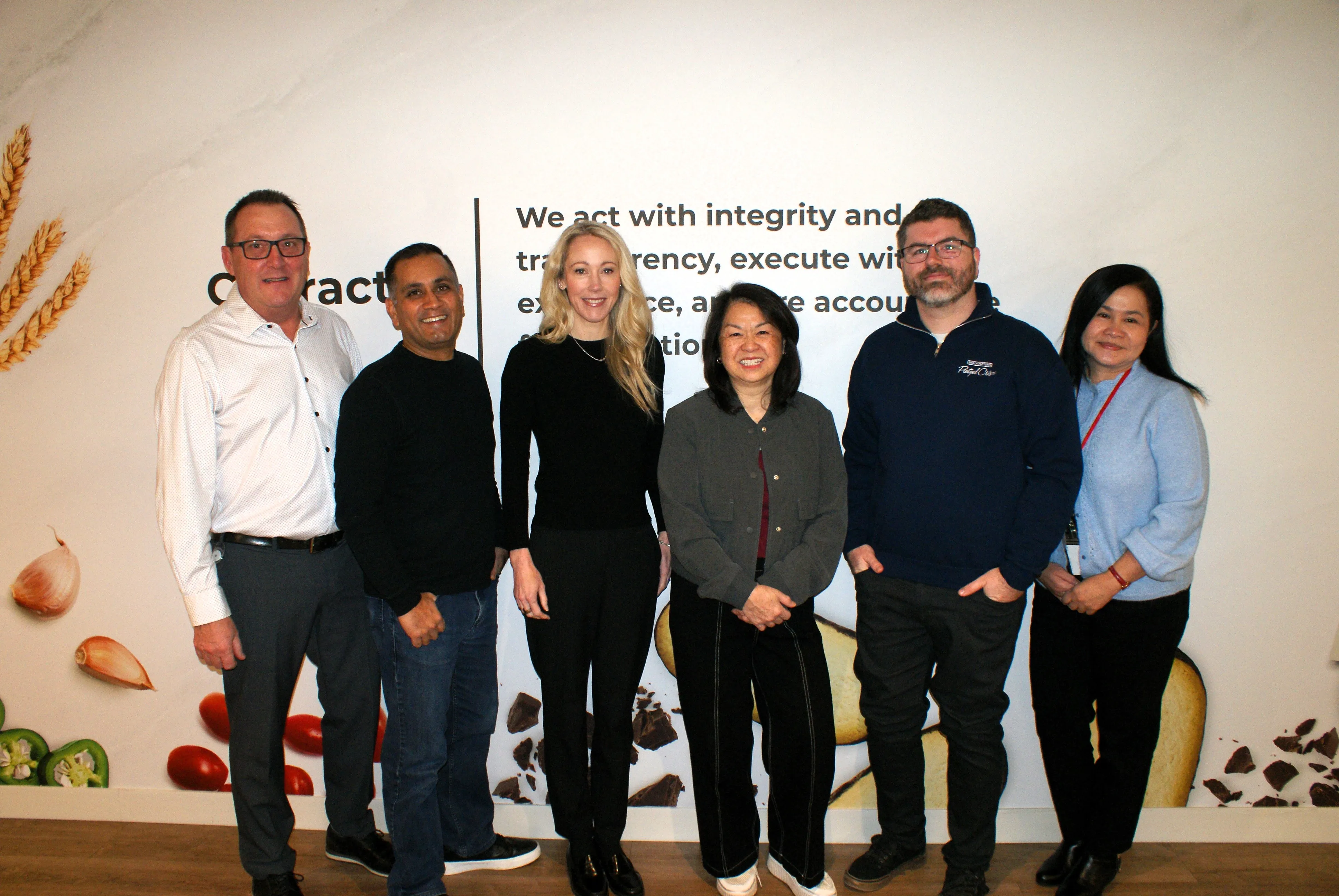 A smiling Campbell's employee in a factory setting holds a package of Disney Mickey Mouse Goldfish crackers while pointing towards the production line