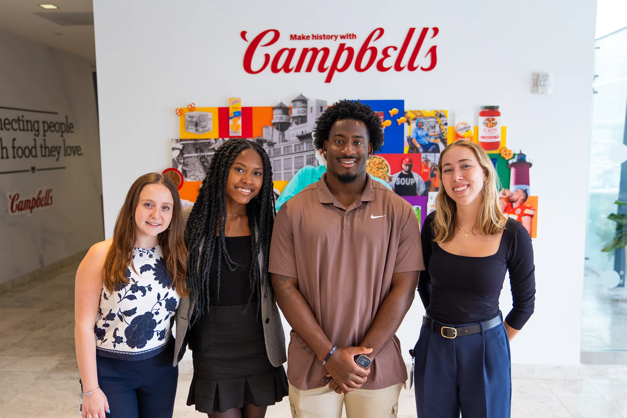 Four Campbell's interns smiling for a photo in front of a company mural