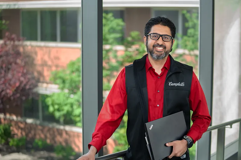 A smiling man in a Campbells vest holds a laptop