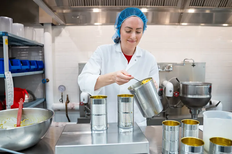 A scientist in a lab coat fills empty cans with product as part of the research and development process