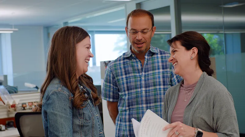 Three smiling colleagues discuss legal documents in an office