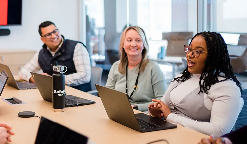 Diverse group of smiling professionals collaborating around a conference table with laptops