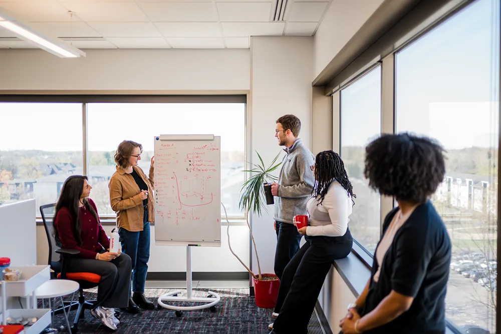 A diverse group of marketing professionals collaborating and discussing ideas around a whiteboard in a bright office