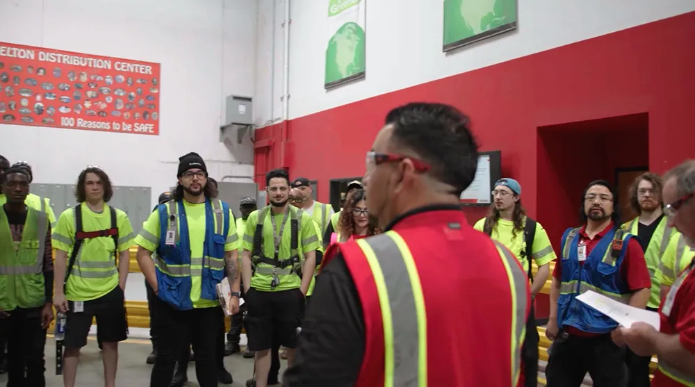 A team of warehouse employees is listening to a manager during a safety meeting in a distribution center.