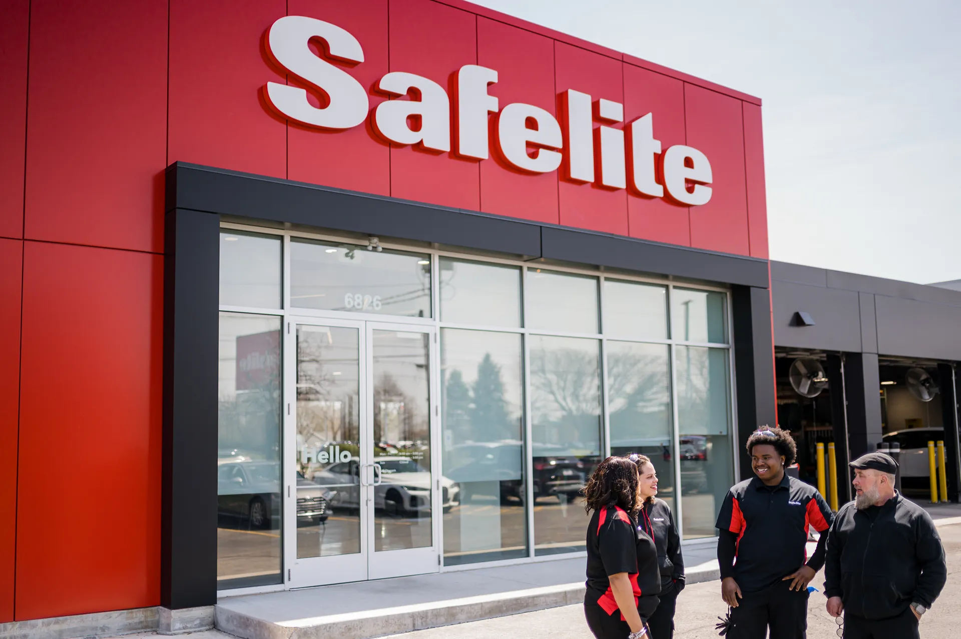 Three Safelite employees talking outside a store with a large red sign.