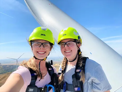 A paif of women taking a selfie on top of a wind turbine