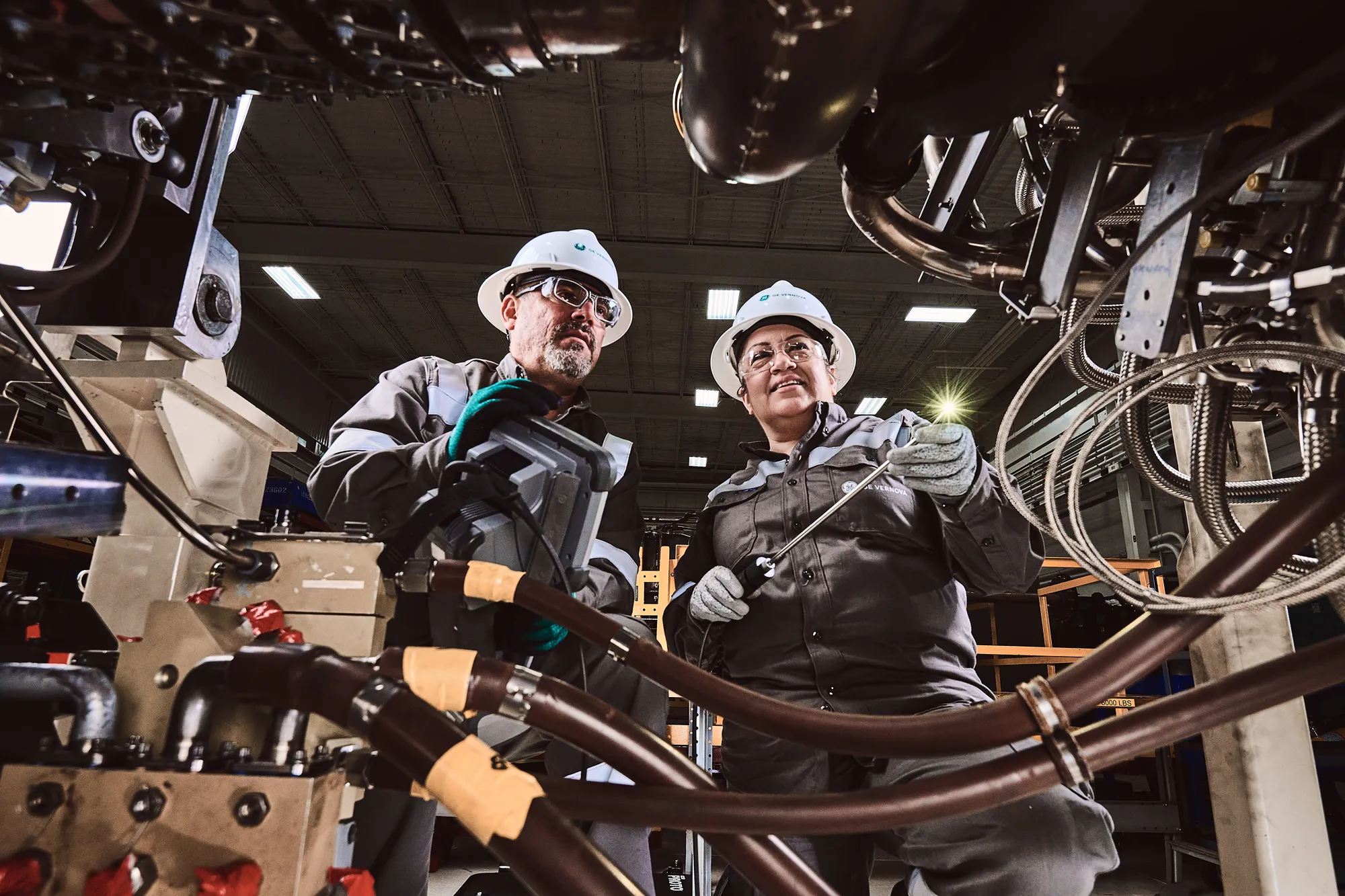 A photo of two people in safety gear working in a large piece of machinery