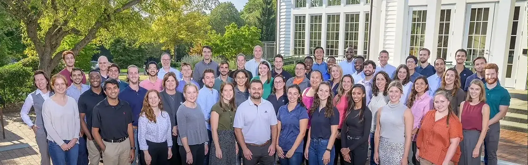 A group of people stand outside a white building and pose for a group photo