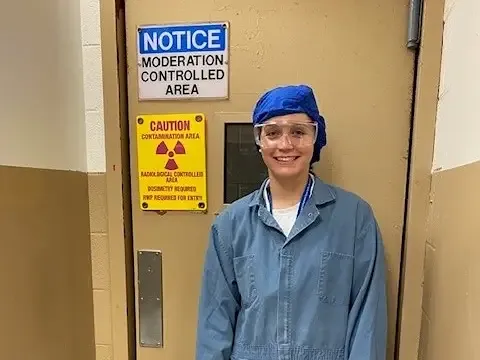 A woman standing outside of a door marked with various warning signs