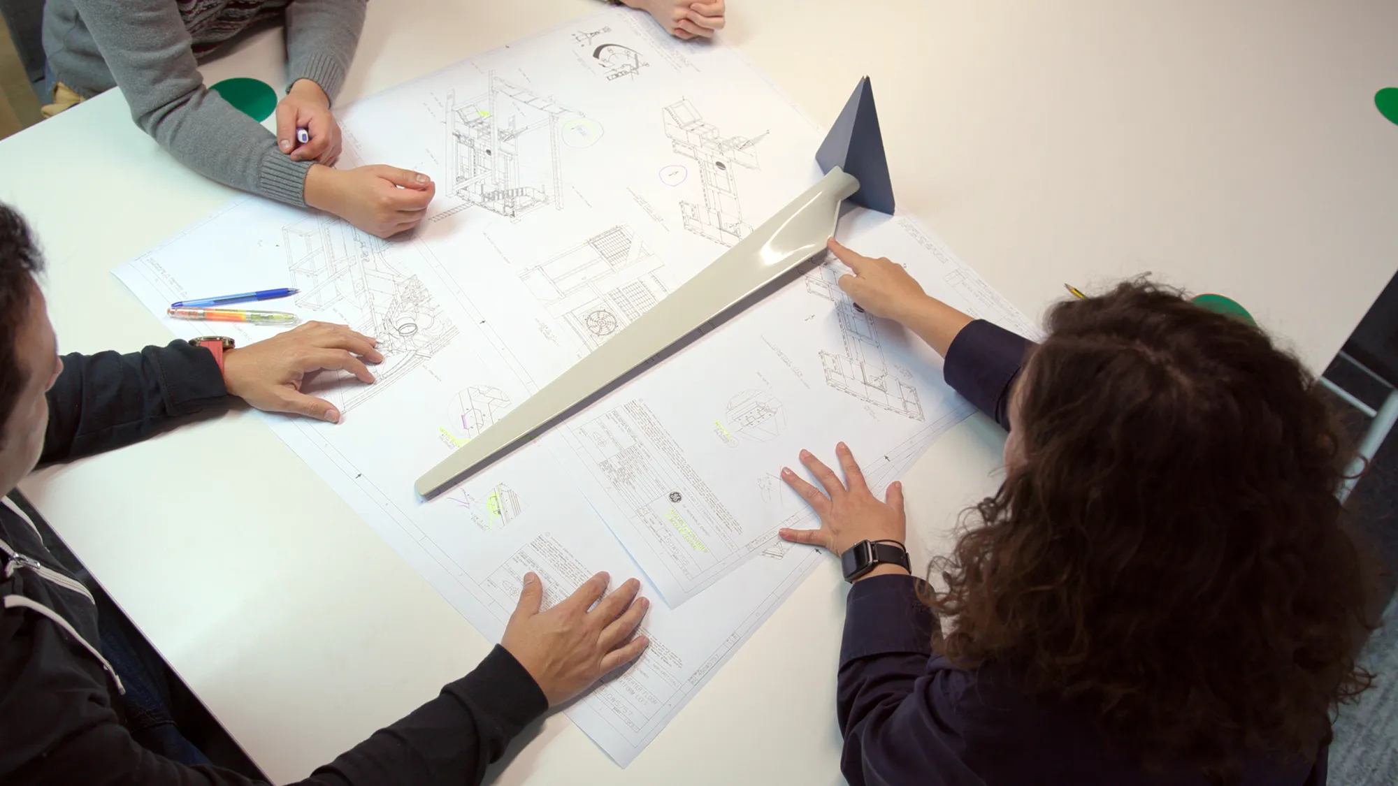 A group of people standing around a table containing a set of schematics
