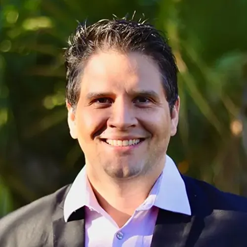 A photo of a man in a blue jacket smiling with nature behind him