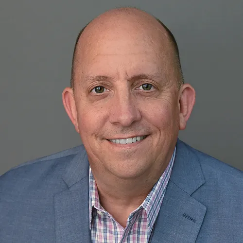 A photo of a man wearing a blue jacket in front of grey background