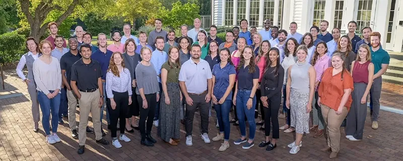 A group of people pose for a photo outside of a large white building