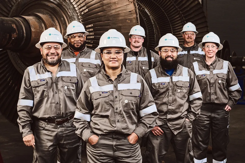 A group of people wearing safety gear stand in front of a large machine