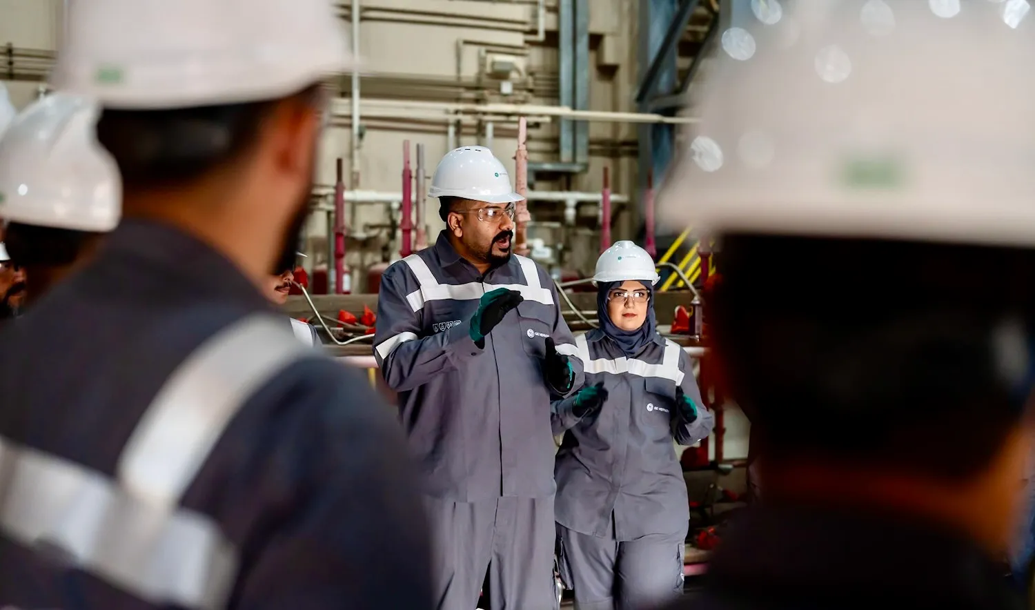 A man on a factory floor gives instructions to a group of people