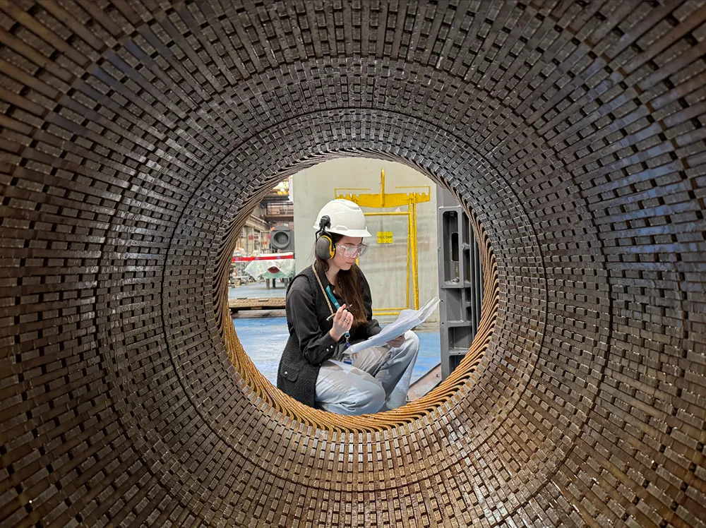 A woman wearing a hardhat and ear protetection looks over documents