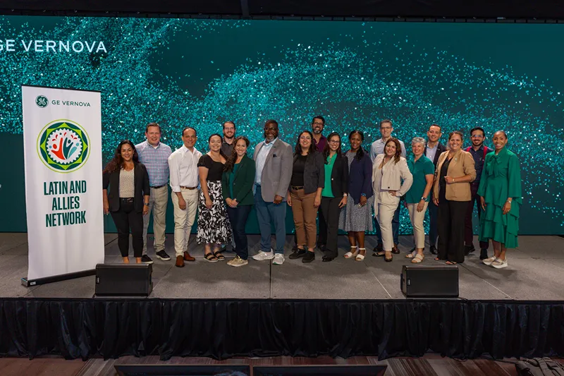 A group of people stand on stage next to a banner that reads Latin and Allies Network