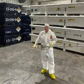 A woman wearing a white lab coat and protective clothing holding a long metal tool