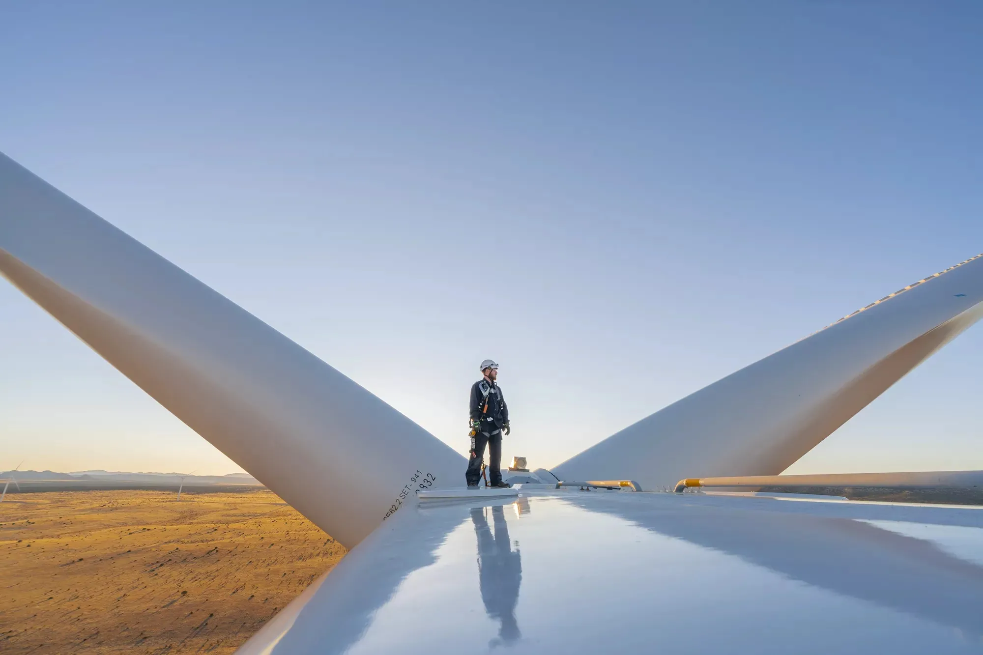 A photo of a man standing atop of a wind turbine