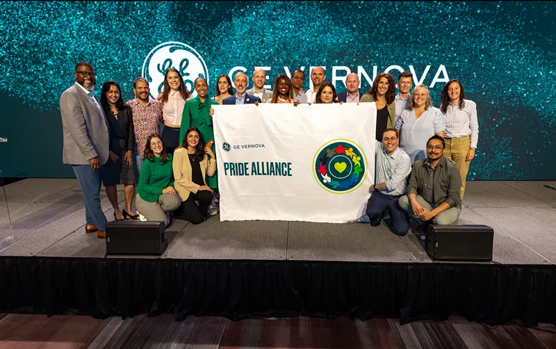A group of people stand on stage next to a banner that reads Pride Alliance