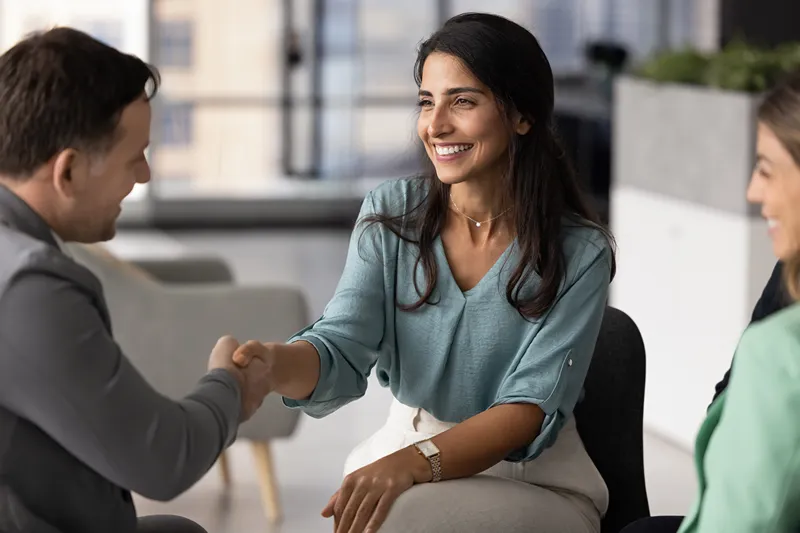 A woman shaking hands with a man sitting in an office