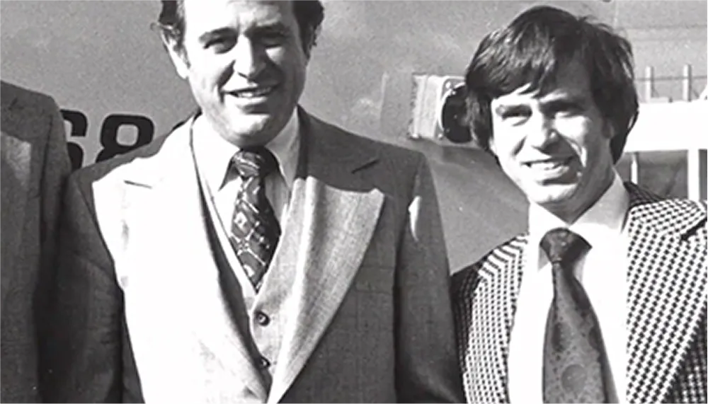 Two men in suits smiling in front of an aircraft