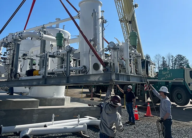 A group of 3 men using a crane to lift a heavy piece of machinery