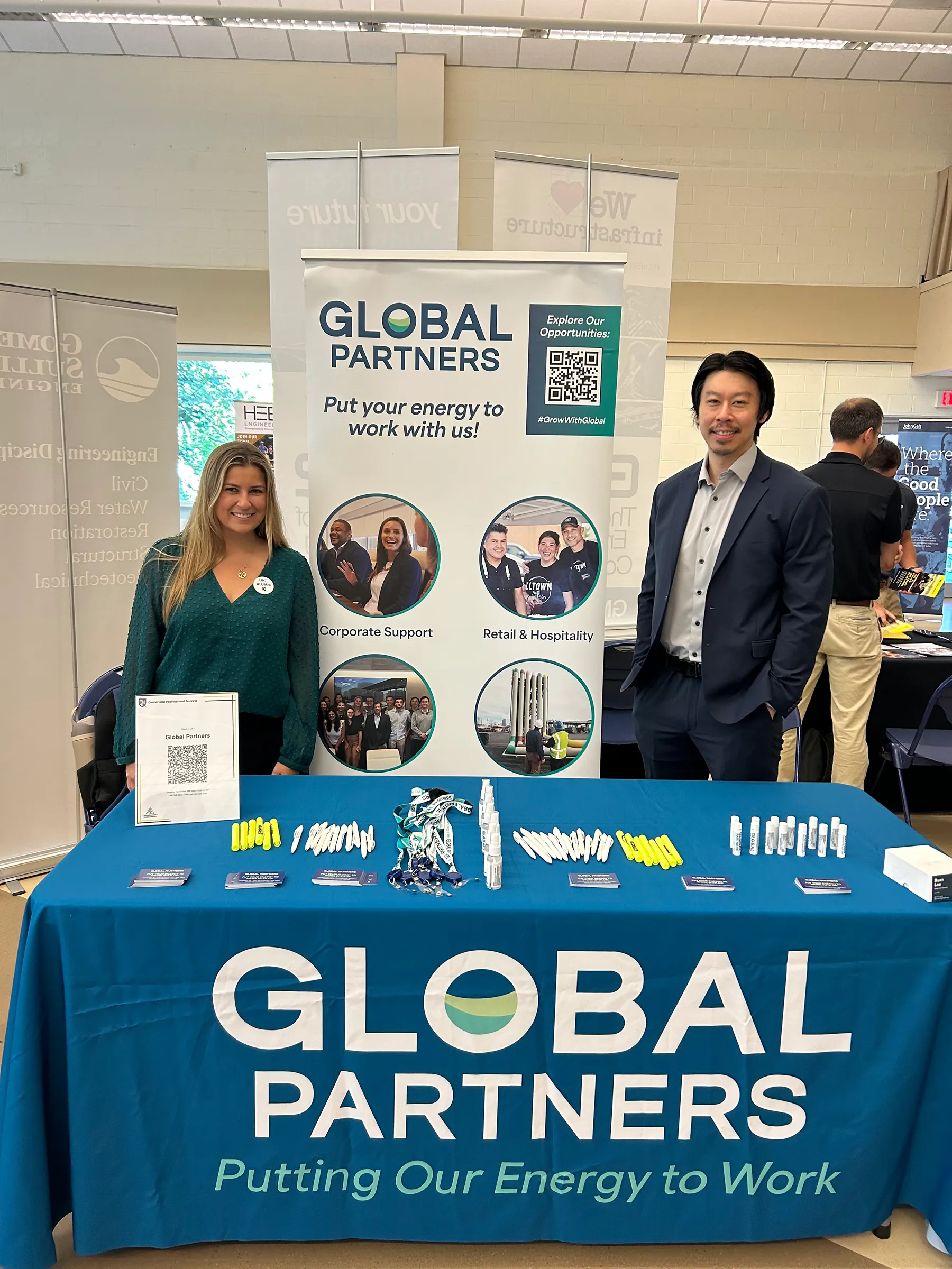 Two people standing at a table containing Global Partners branded items