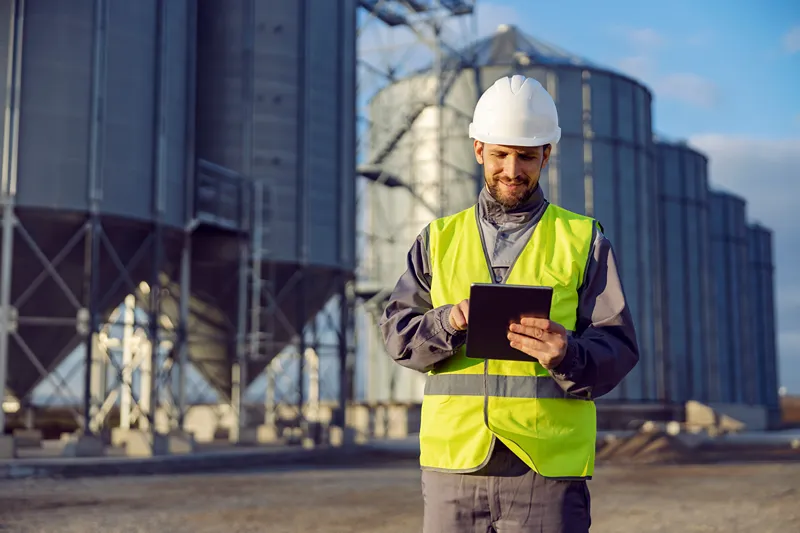A man looking at his tablet wearing a safety vest and hard hat