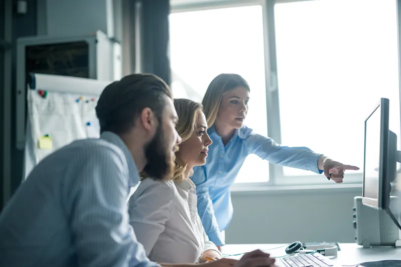Three people in an office looking at a computer screen, with one person pointing