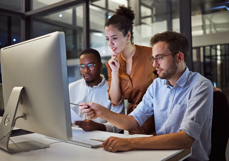 Three people in an office looking at a computer screen, with one person pointing