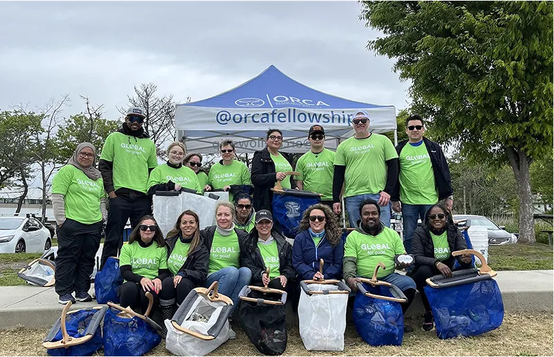 A group of 17 people in green shirts poses with collection bags