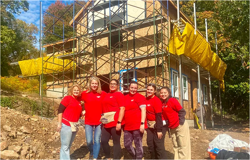 A group of people posing for a photograph with the image of a house being built in the background