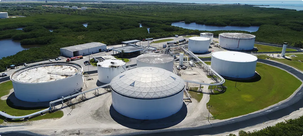 Aerial view of an industrial storage tank facility surrounded by greenery and water