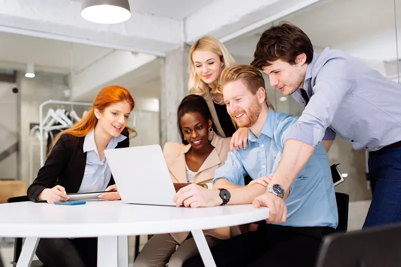 A group of people sitting around a table looking at a laptop computer