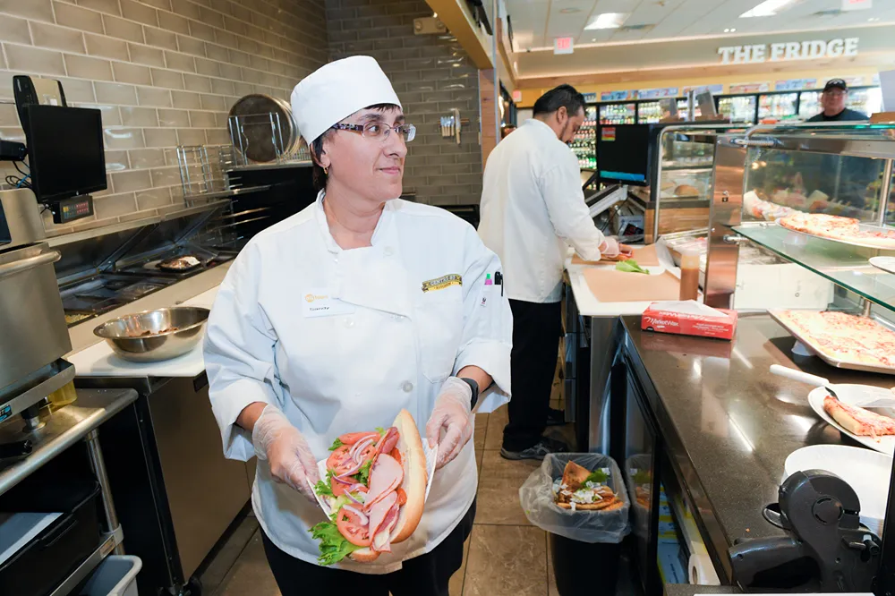 A chef prepares a submarine sandwhich in a kitceh