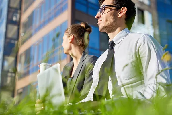 Two people sitting in grass near a modern glass building