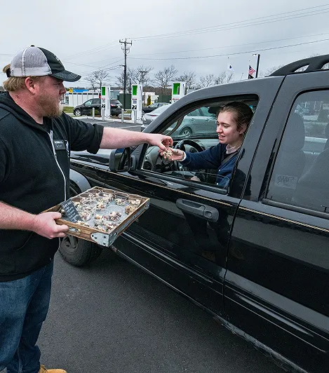 A person giving away food samples to a person in their vehicle
