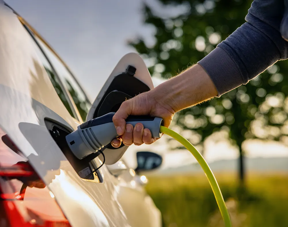 A person is plugging an electric vehicle (EV) charging cable into a car outdoors.