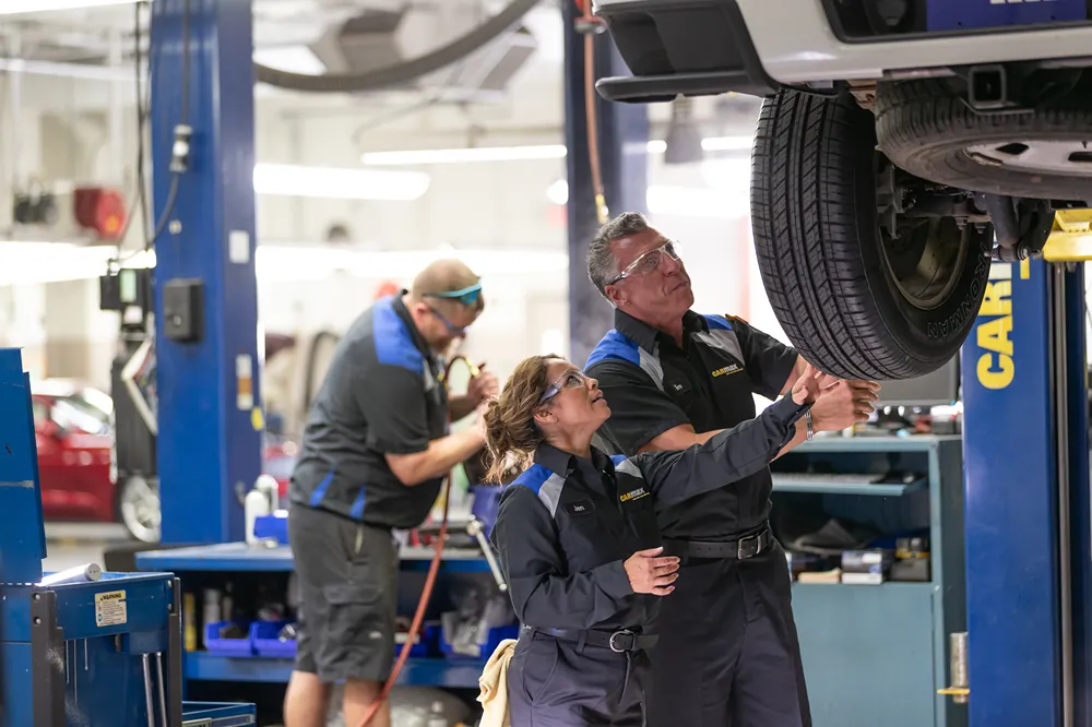 Smiling CarMax employee meeting with a customer in a bright office, discussing paperwork at a desk.