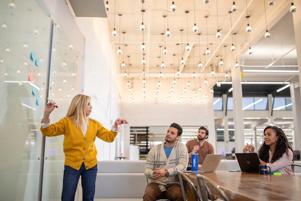 A diverse group of students or employees is attending a brainstorming session led by a woman at a whiteboard.