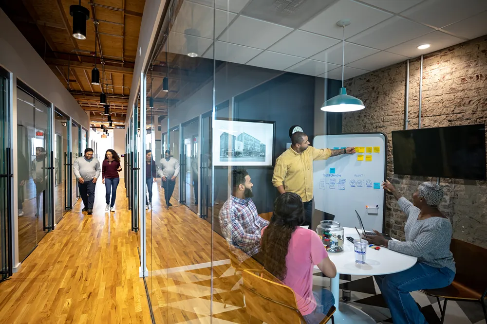 Smiling CarMax employee meeting with a customer in a bright office, discussing paperwork at a desk.