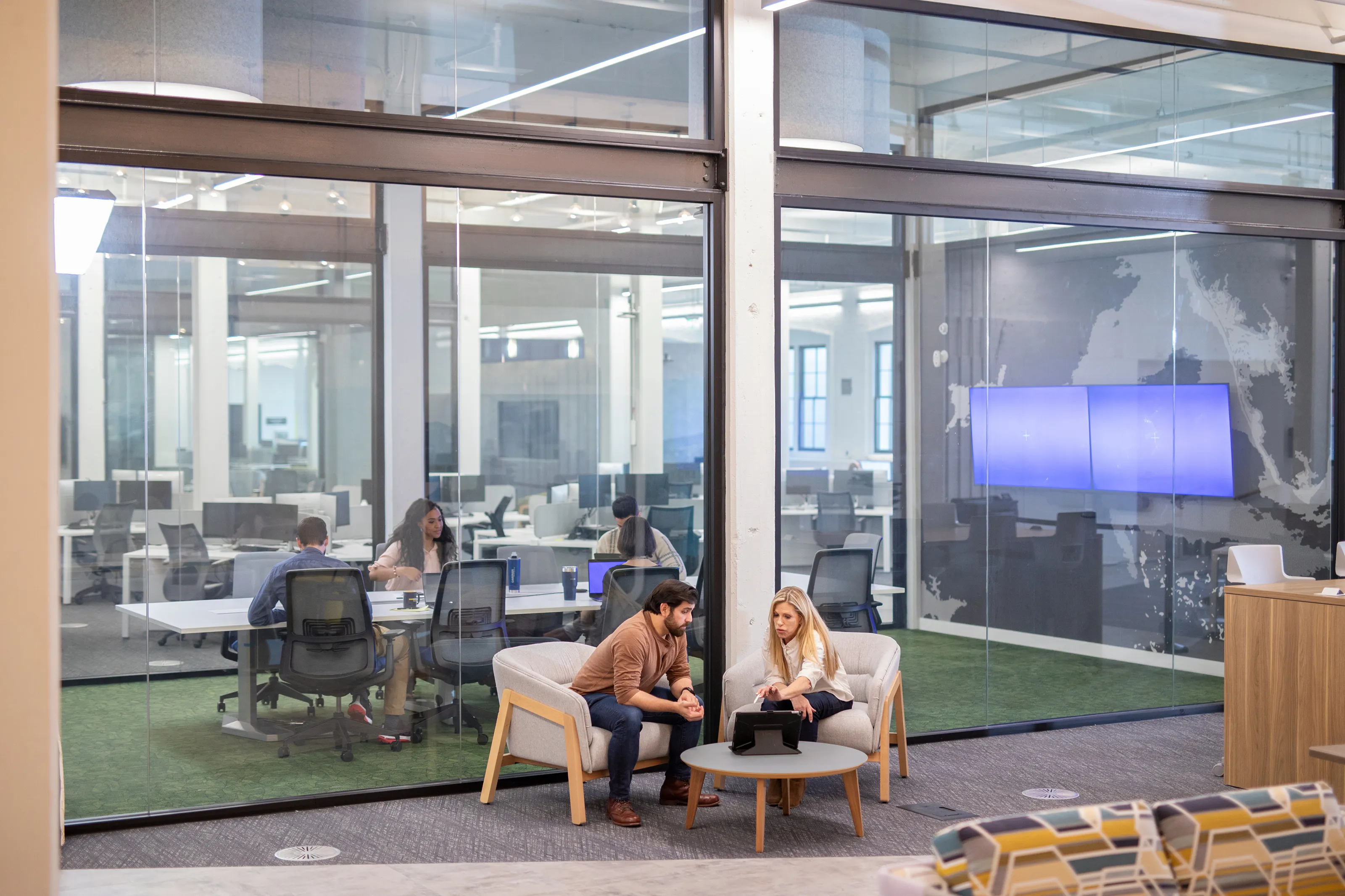 Two colleagues are having a relaxed discussion in a bright, modern office lounge area.