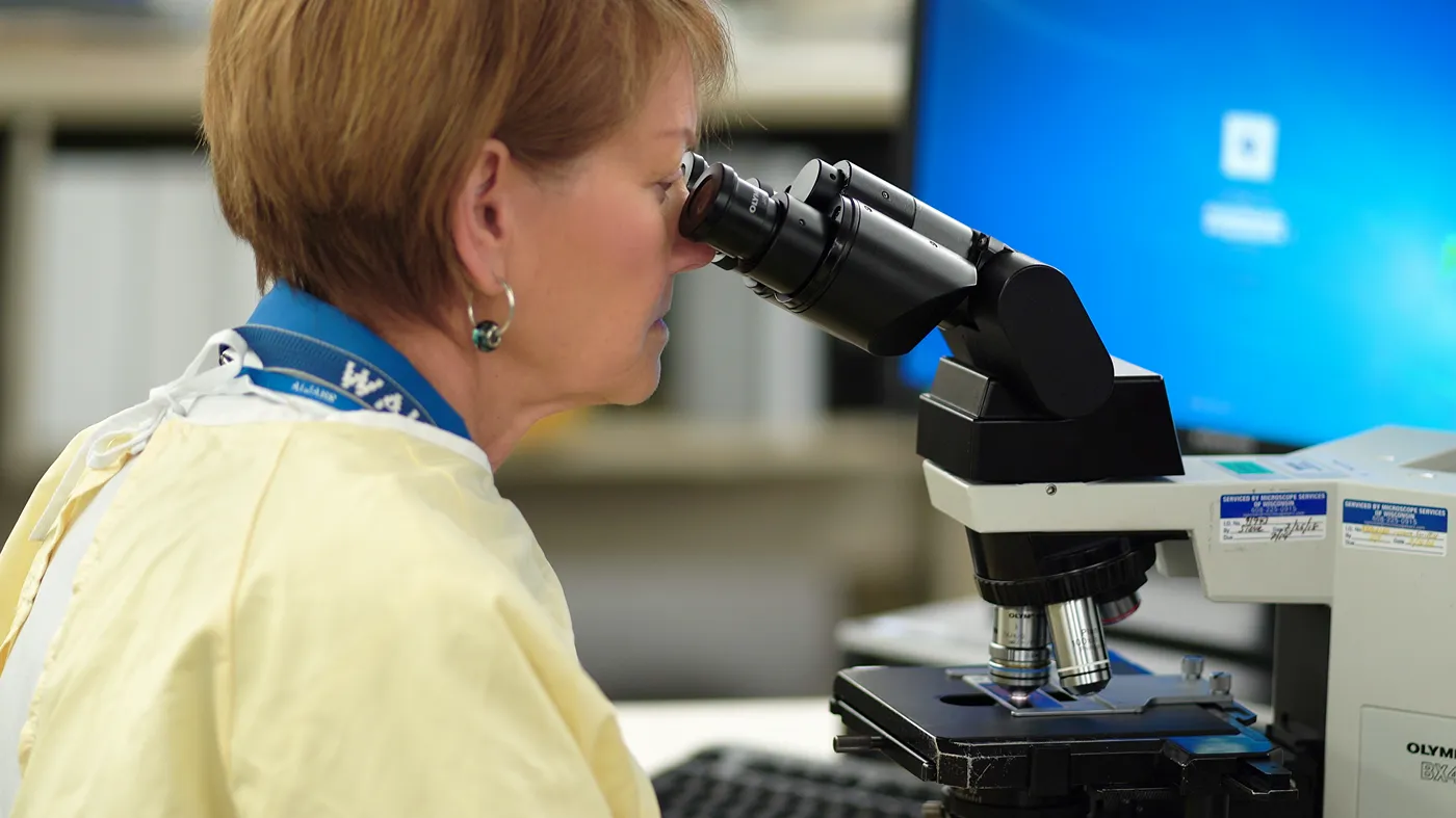 Medical laboratory technician examining sample under microscope in research lab