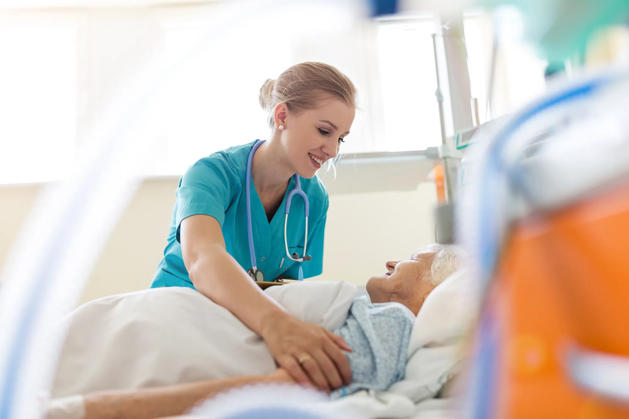 A photo of a female nurse standing over the bedside of an elderly female patient