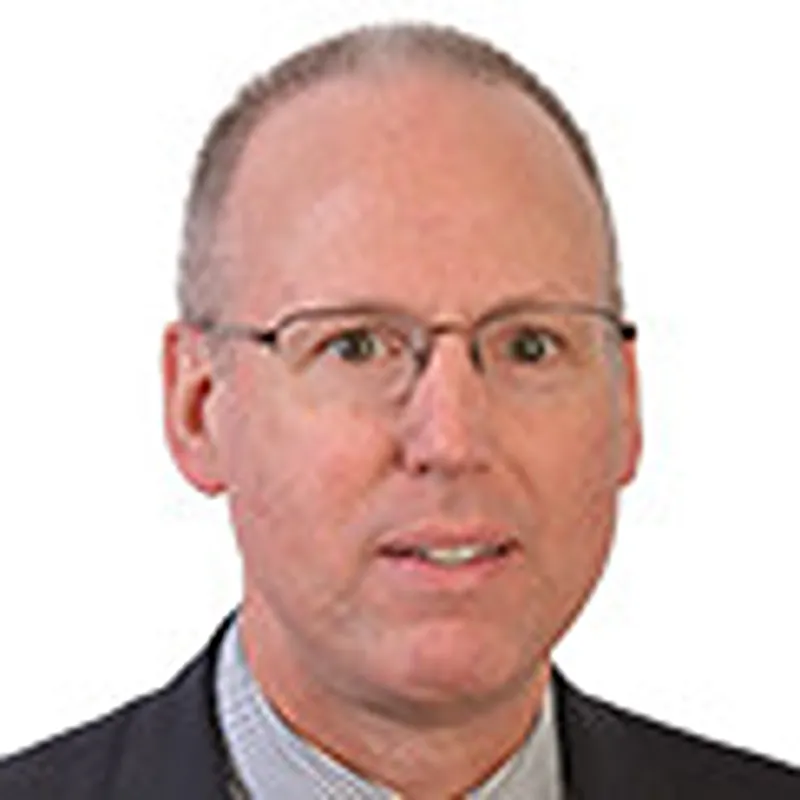 Headshot of Patrick Coplan, a man with glasses wearing a suit and looking forward