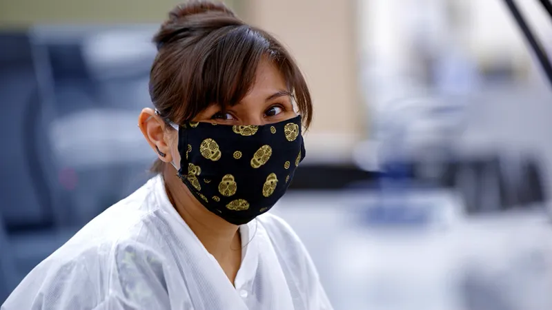 A closeup photo of a woman wearing a medical face mask looking into the camera