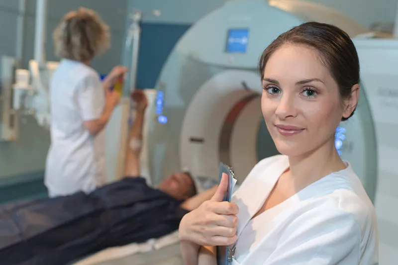 Smiling radiology technician gives thumbs up in a modern CT scanning room with a patient